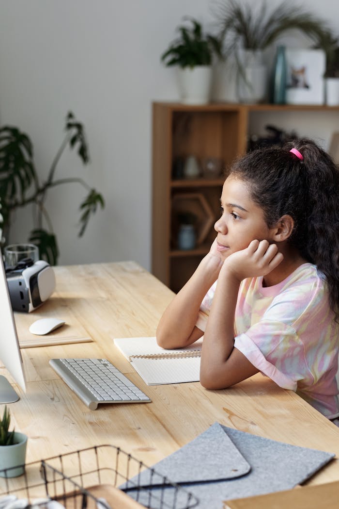 Girl studying online at home, concentrating on computer screen with hands on cheeks.